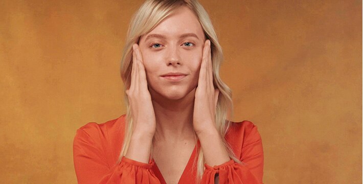 woman applying cream on an orange background