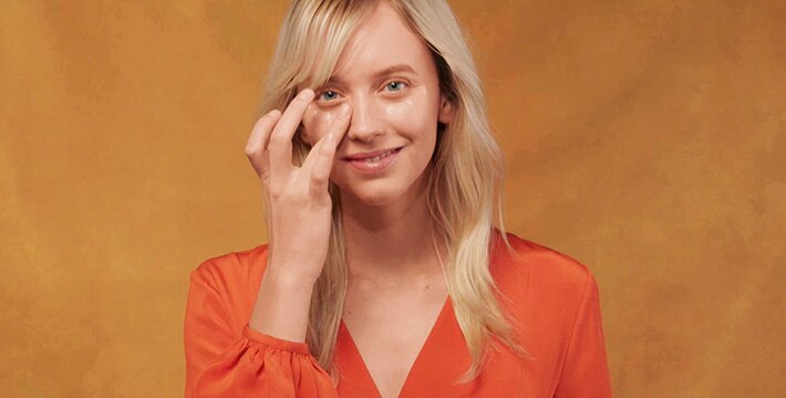 woman applying eye cream on an orange background
